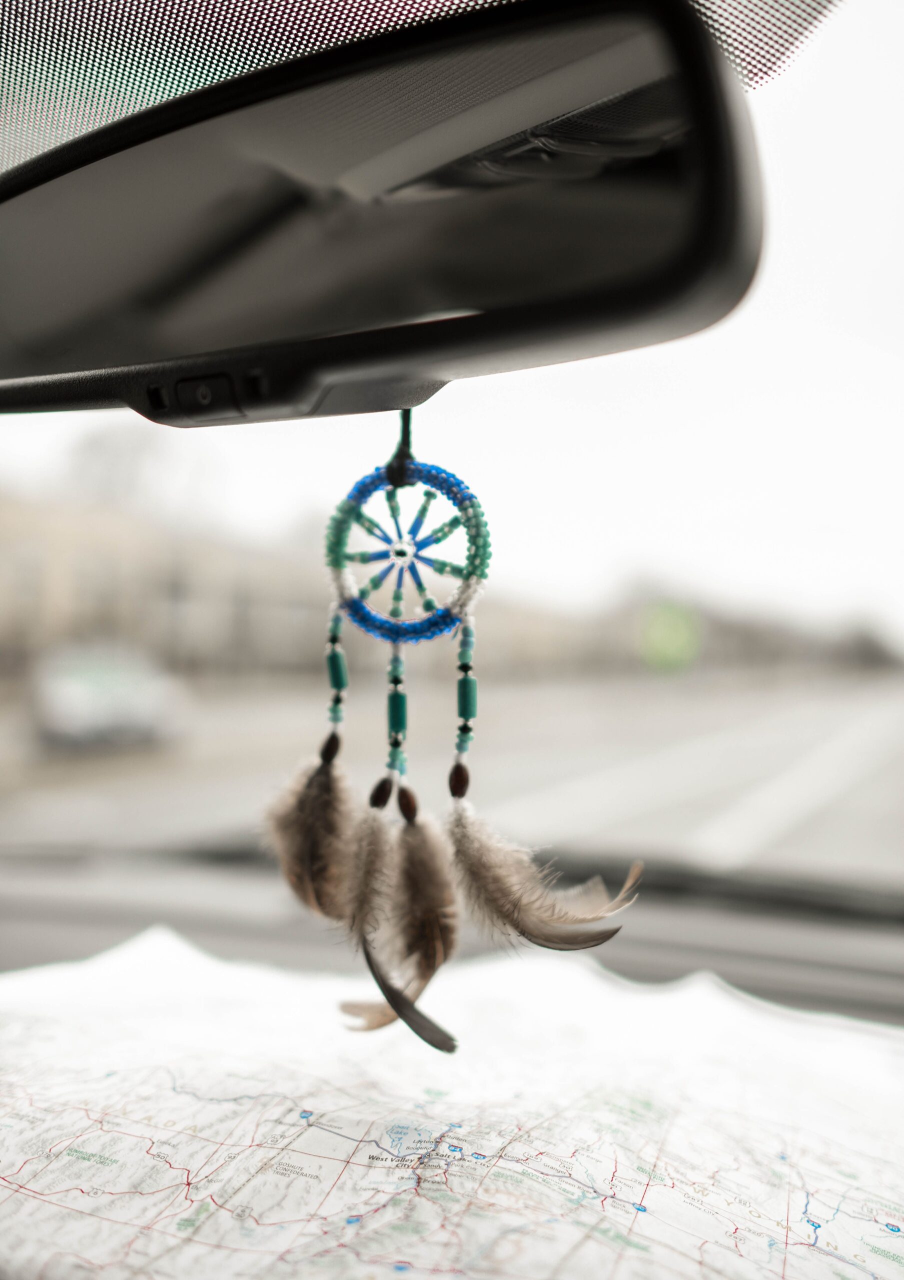 Part of car interior with little dreamcatcher hung as rearview mirror pendant above unfolded map